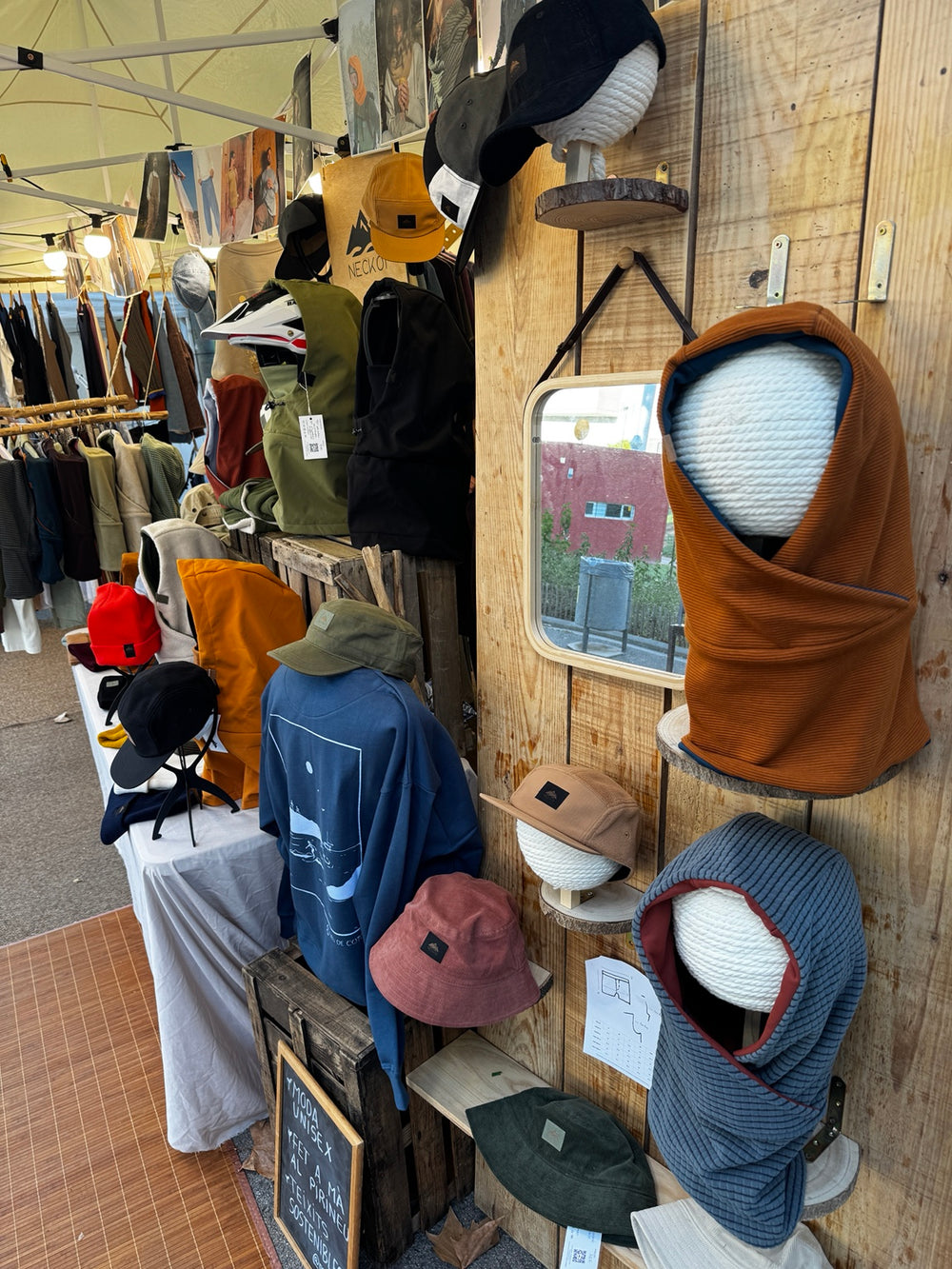 Cagoules, casquettes et bonnets Neckoi sur un présentoir en bois à côté d’un miroir